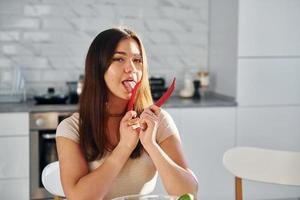 una mujer muy joven con ropa informal se sienta en la cocina con pimiento rojo foto