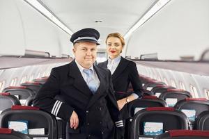 Pilot in uniform and stewardess is standing inside of airplane photo