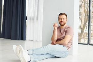 Man in casual clothes is sitting on the floor in modern domestic room photo