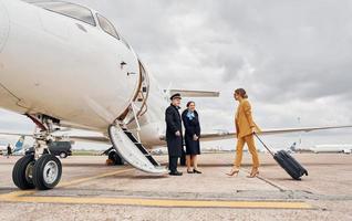 Airplane crew leads woman in yellow clothes inside of a plane photo