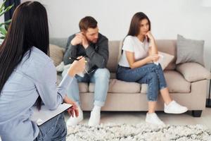 Couple is sitting on the sofa and working with female psychologist photo