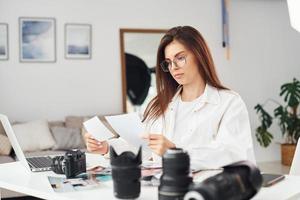 Female photographer in casual clothes is working indoors at daytime photo