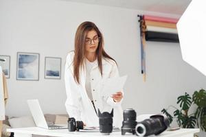 Female photographer in casual clothes is working indoors at daytime photo