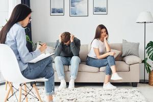 Couple is sitting on the sofa and working with female psychologist photo