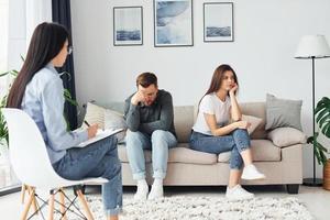 Couple is sitting on the sofa and working with female psychologist photo