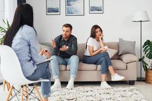 Couple is sitting on the sofa and working with female psychologist photo