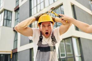 Standing near modern buildings. Young man working in uniform at construction at daytime photo