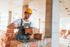 Yellow colored hard hat. Young man working in uniform at construction at daytime photo