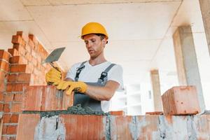 Working by using bricks. Young man in uniform at construction at daytime photo