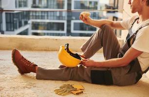 Sitting on the floor. Young man working in uniform at construction at daytime photo