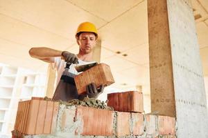 Yellow colored hard hat. Young man working in uniform at construction at daytime photo