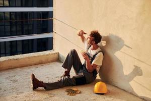 Sitting on the floor. Young man working in uniform at construction at daytime photo
