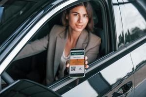 con pasaporte de vacunas. mujer probando auto nuevo. sentado en el interior de un automóvil moderno foto