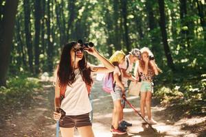chica parada frente a sus amigos. niños paseando por el bosque con equipo de viaje foto
