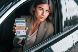 con pasaporte de vacunas. mujer probando auto nuevo. sentado en el interior de un automóvil moderno foto