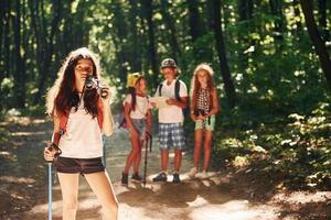 Girl standing in front of her friends. Kids strolling in the forest with travel equipment photo