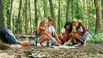 Sitting on the ground. Kids strolling in the forest with travel equipment photo