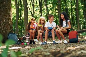 Sitting and having a rest. Kids strolling in the forest with travel equipment photo