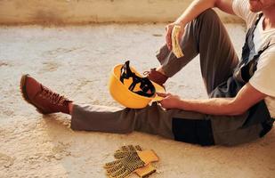 Sitting on the floor. Young man working in uniform at construction at daytime photo