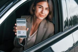 con pasaporte de vacunas. mujer probando auto nuevo. sentado en el interior de un automóvil moderno foto