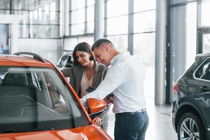 Orange colored car. Man in formal wear helping customer with choice of the automobile photo