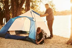 Father and son installing tent outdoors near the lake photo