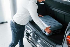 Conception of tourism. Man in formal clothes is with luggage indoors near the car photo