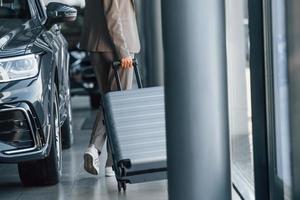 Holding luggage. Woman is indoors near brand new automobile indoors photo