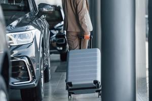 Holding luggage. Woman is indoors near brand new automobile indoors photo