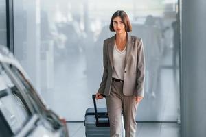 Posing for a camera. Woman with luggage is standing indoors. Conception of tourism photo