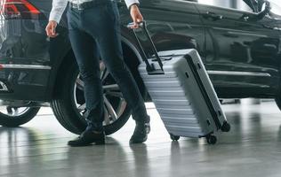 Partical view. Man in formal clothes is with luggage indoors near the car photo