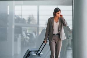 Talking by phone. Woman with luggage is standing indoors. Conception of tourism photo