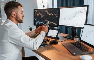 Graphs and diagrams. Young businessman in formal clothes is in office with multiple screens photo