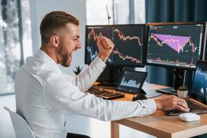 Using laptop. Young businessman in formal clothes is in office with multiple screens photo