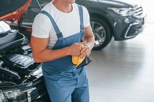 In blue uniform. Man is repairing broken automobile indoors photo