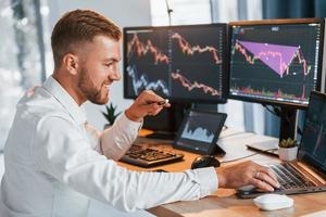 Using laptop. Young businessman in formal clothes is in office with multiple screens photo