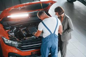 Woman in stylish clothes. Man repairing woman's automobile indoors. Professional service photo