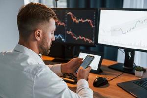 Young businessman in formal clothes is in office with multiple screens. Conception of exchange photo