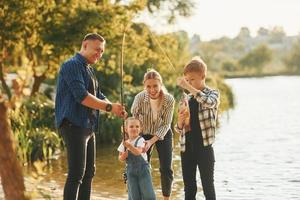 At summertime. Father and mother with son and daughter on fishing together outdoors photo