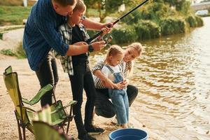 Learning to fishing. Father and mother with son and daughter together outdoors at summertime photo