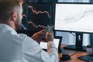 Graphs is going down. Young businessman in formal clothes is in office with multiple screens photo