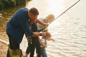 Learning to fishing. Father and mother with son and daughter together outdoors at summertime photo
