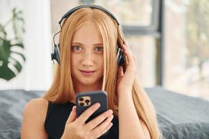 In headphones. Female teenager with blonde hair is at home at daytime photo