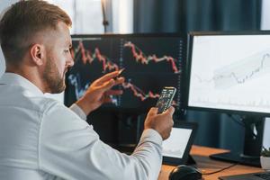 Graphs is going down. Young businessman in formal clothes is in office with multiple screens photo