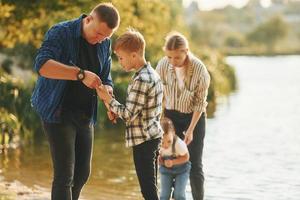 In casual clothes. Father and mother with son and daughter on fishing together outdoors at summertime photo