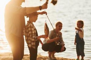 In casual clothes. Father and mother with son and daughter on fishing together outdoors at summertime photo