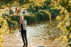 With good catch. Boy in casual clothes in on fishion outdoors at summertime photo