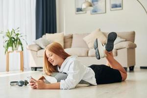 Laying down on the floor. Female teenager with blonde hair is at home at daytime photo
