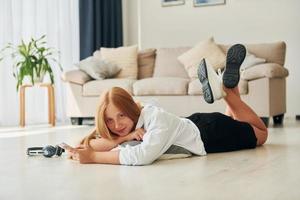 Laying down on the floor. Female teenager with blonde hair is at home at daytime photo