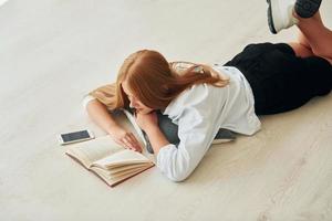 Reading book. Female teenager with blonde hair is at home at daytime photo